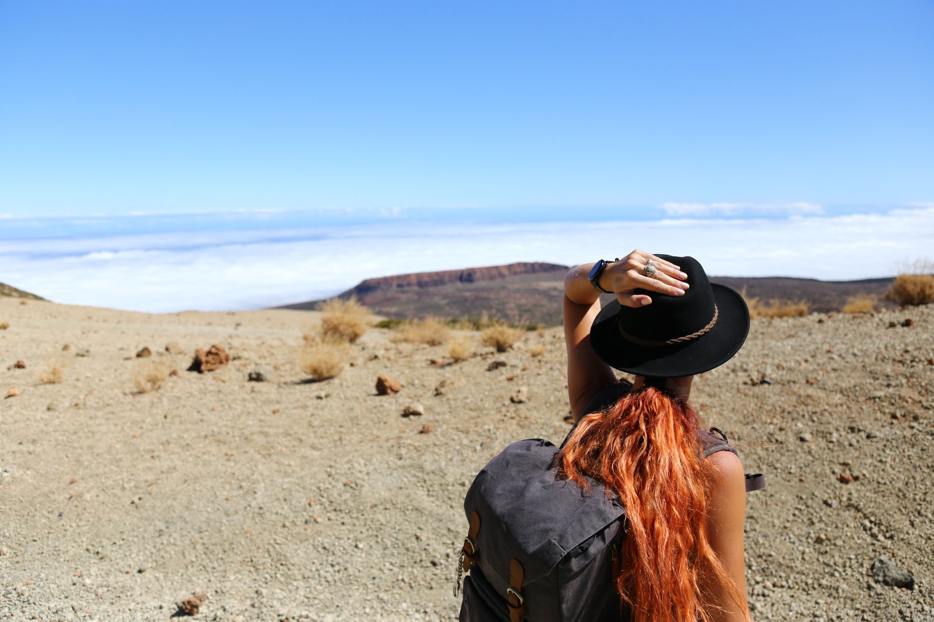 Woman standing in a desert landscape, looking at distant mountains, wearing a hat and backpack.
